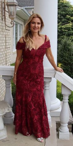 a woman in a long red dress standing on a porch next to a white column