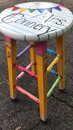 a colorful stool with writing on it sitting in the middle of an asphalt area next to a parking lot