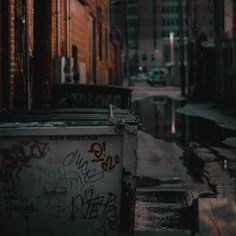 a trash can sitting on the side of a street next to a brick building with graffiti all over it