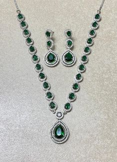 Emerald Diamond Necklace features a striking green faux emerald pendant surrounded by sparkling American diamonds and cubic zirconia. The statement piece reflects the elegance of Indian and Pakistani jewelry, making it a beautiful and culturally rich gift for her. Perfect for special occasions, this jewelry set adds a touch of luxury and timeless beauty to any collection. *𝐏𝐑𝐎𝐃𝐔𝐂𝐓 𝐃𝐄𝐓𝐀𝐈𝐋* * 𝐌𝐚𝐭𝐞𝐫𝐢𝐚𝐥: Brass * 𝐏𝐥𝐚𝐭𝐢𝐧𝐠: White Rhodium Plated * 𝐒𝐭𝐨𝐧𝐞: AAA-quality CZ D Green Jewelry Sets With Diamond Accents For Party, Green Jewelry Sets With Stones For Party, Emerald Jewelry With Diamond Accents For Party, Green Crystal Jewelry Sets With Sparkling Stones, Green Stone Jewelry For Formal Occasions, Green Stone Formal Jewelry, Green Crystal Jewelry Sets With Jewels, Green Round Crystal Jewelry, Green Formal Jewelry With Stones