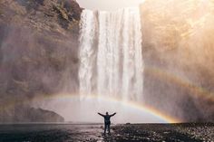 a person standing in front of a waterfall with a rainbow