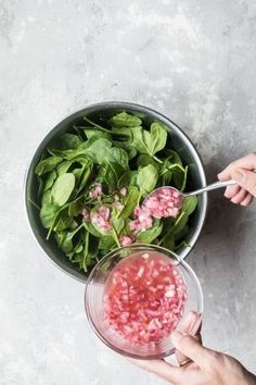 two hands holding a bowl of spinach and another hand with a spoon