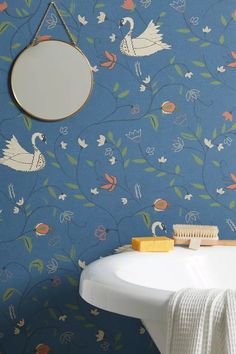 a white sink sitting under a mirror next to a blue wall with flowers and swans on it