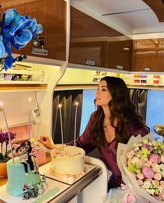 a woman sitting in front of a table with cake and flowers on it, surrounded by candles