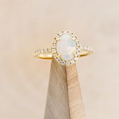 an opal and diamond ring sits on top of a wooden stand in front of a beige background