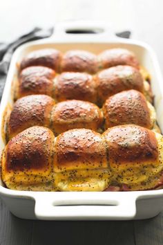 a white casserole dish filled with bread and cheese on a wooden table next to a black napkin