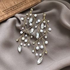 a pair of white and gold earrings on top of a gray cloth next to a wooden box