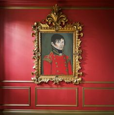 a portrait of a man in uniform hangs on a red wall with gold trimmings