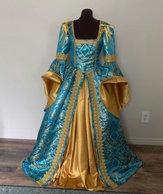 This striking gown is made from a vibrant turquoise blue, designer damask with a ornate gold pattern woven throughout.  The bodice features a deep, square neckline trimmed with gold braid to accentuate your decoletage. The gathered overskirt is firmly attached to the bodice, and is also trimmed with a stunning wide braid down the skirt fronts for a lovely elegant line.   The dramatic great sleeves are trimmed with the wide gold braid at the elbow, and the wide bell sleeves can be turned back to reveal the gorgeous gold lining.  The sleeves can be made attached or detachable. Closes at the back through brass grommets which allows for a more adjustable fit, and backed with a modesty panel. This bodice is boned along the front/side seams and at the grommet back closure. The gold underskirt is Royal Blue Gown With Fitted Bodice, Blue Dress With Historical Design And Fitted Bodice, Blue Baroque Dress With Historical Design, Blue Gown With Fitted Bodice For Costume Party, Blue Brocade Wedding Dress, Blue Baroque Costume Dress, Blue Historical Dress For Costume Party, Blue Historical Costume Party Dress, Blue Historical Design Dress For Costume Party