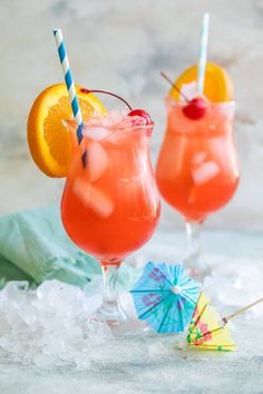 two cocktails with orange slices and umbrellas on ice