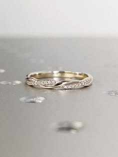 a gold wedding band with white diamonds on a silver surface and drops of water around it