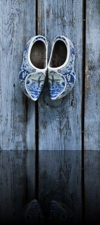 pair of blue and white shoes hanging on wooden door with boat scene painted on them