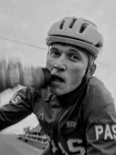 black and white photograph of a man wearing a helmet riding a bike with his mouth open