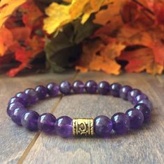 a purple beaded bracelet with a gold clasp on it and leaves in the background