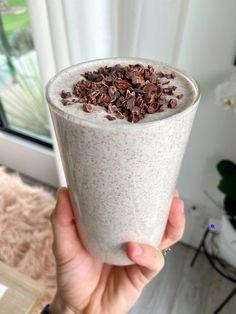 a person holding up a drink with chocolate chips on top in front of a window