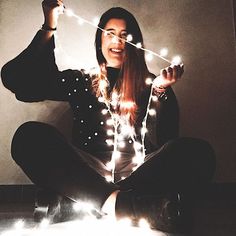 a woman sitting on the floor holding up string lights