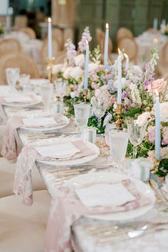 the table is set with white and pink flowers, candles, and napkins on it