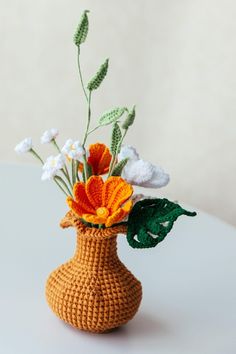 a crocheted vase filled with flowers on top of a white table next to a wall