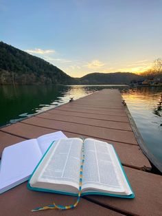 an open book sitting on top of a wooden dock next to the water at sunset