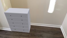 a white dresser sitting in the corner of a room next to a wall with a light shining on it