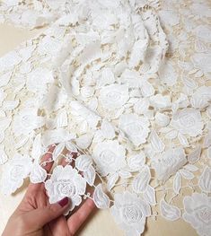 a person is holding an object in their hand on a table with white lacy material