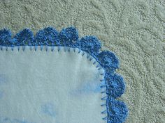 a close up of a blue and white doily on a quilted material with crocheted edges