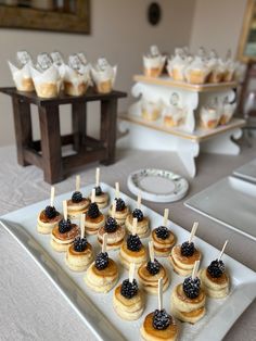 small desserts are arranged on a white plate with toothpicks and blackberries