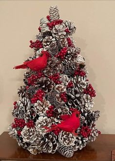 a christmas tree made out of pine cones and red berries with two cardinal birds on top