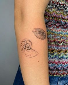 a woman's arm with two seashells tattoo on the left side of her arm