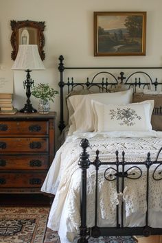 a bed with white linens and pillows in a bedroom next to a lamp, dresser and mirror