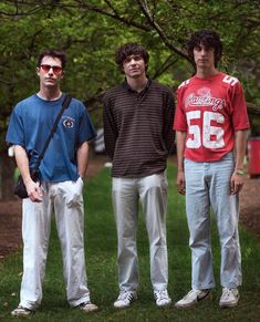 three young men standing next to each other in front of a tree and grass area