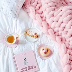 a pink blanket, cupcakes and tea on a bed with a white comforter