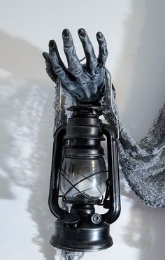 a creepy hand holding an old fashioned lantern on top of a white table with a gray scarf around it