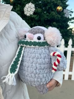 a person holding a crocheted stuffed animal in front of a christmas tree