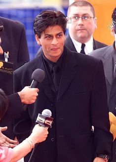 a man in a suit and tie holding a microphone while standing next to other people