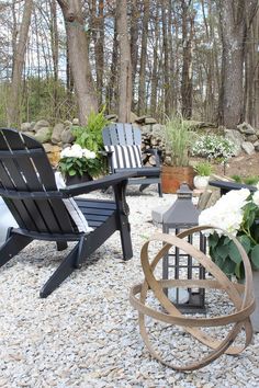 two black chairs sitting on top of a gravel covered ground next to flowers and trees