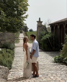 a man and woman standing in front of an iron gate on a cobblestone walkway