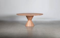 a round wooden table sitting on top of a cement floor next to a white wall