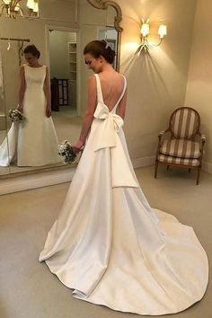 a woman standing in front of a mirror wearing a white dress with a bow on the back