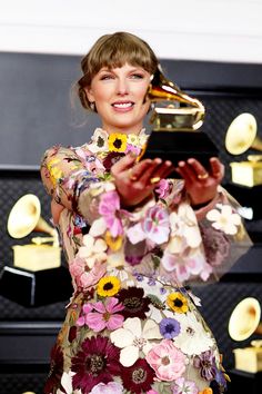 a woman in a floral dress holding an award and looking at the camera with her hands