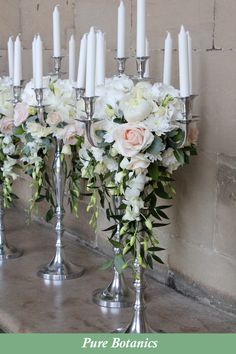 two silver candelabras filled with white flowers and candles