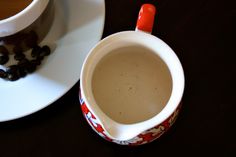 a cup and saucer sitting on a table next to a plate with coffee beans