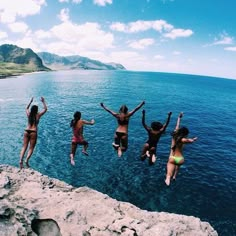 four girls jumping into the water from rocks in front of their backs and arms up