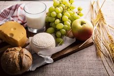 an assortment of cheeses, fruits and milk on a cutting board with some ears of wheat