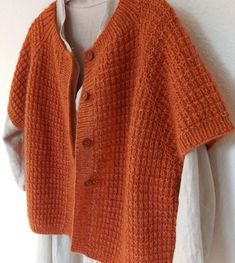 an orange knitted cardigan hanging on a white wall