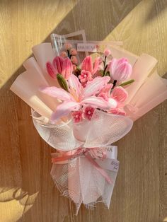 a bouquet of pink flowers on top of a white ribbon tied to a wooden wall