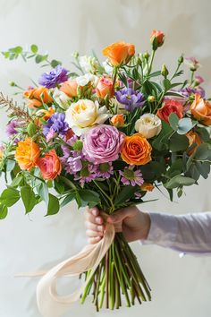 a person holding a bouquet of flowers with ribbons on their hands and wearing a purple shirt