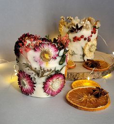 two cakes decorated with flowers and orange slices on a white surface next to some string lights