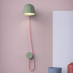 a pink wall with a green lamp on the side and two blue vases next to it