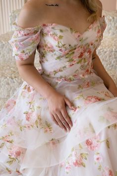 a woman sitting on a couch wearing a dress with flowers all over it and a tattoo on her neck